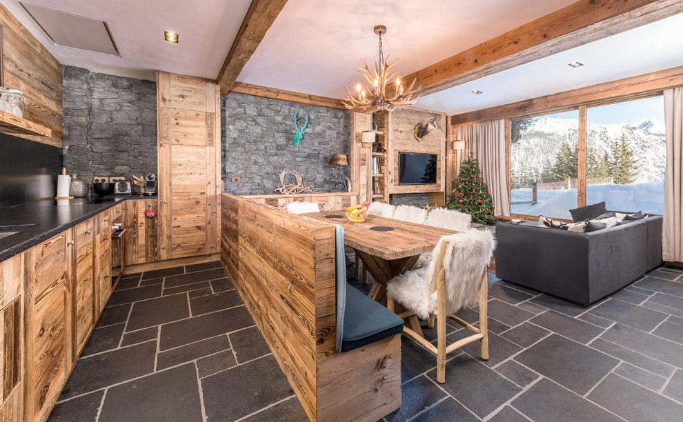 Exemple d'une salle à manger ouverte sur le salon montagne de taille moyenne avec un sol en ardoise, une cheminée standard, un manteau de cheminée en bois et un sol gris.