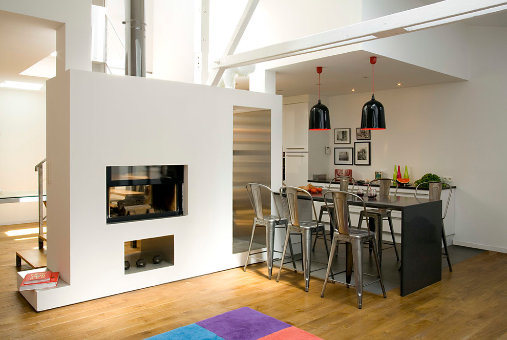Foto de comedor urbano abierto con paredes blancas, suelo de madera en tonos medios y chimenea de doble cara