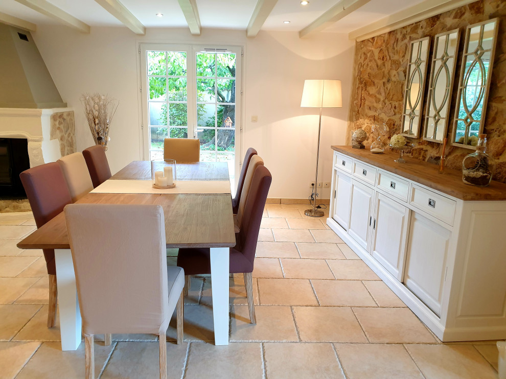 Exemple d'une grande salle à manger chic fermée avec un mur blanc, tomettes au sol, une cheminée standard, un sol beige et poutres apparentes.
