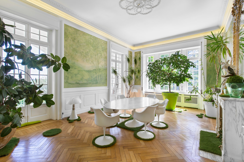 Inspiration pour une salle à manger design avec un mur vert, un sol en bois brun, une cheminée standard, un manteau de cheminée en pierre, un sol marron et éclairage.