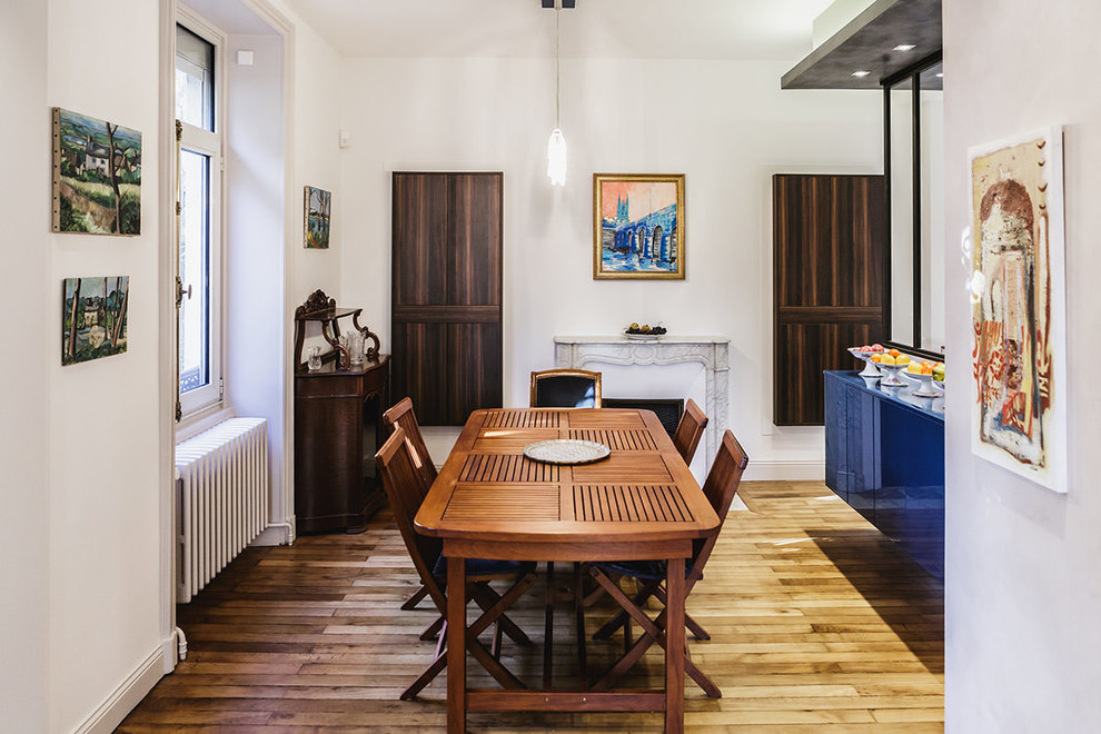 Cette image montre une salle à manger ouverte sur le salon minimaliste de taille moyenne avec un mur beige, un sol en bois brun, une cheminée standard, un manteau de cheminée en pierre et un sol beige.