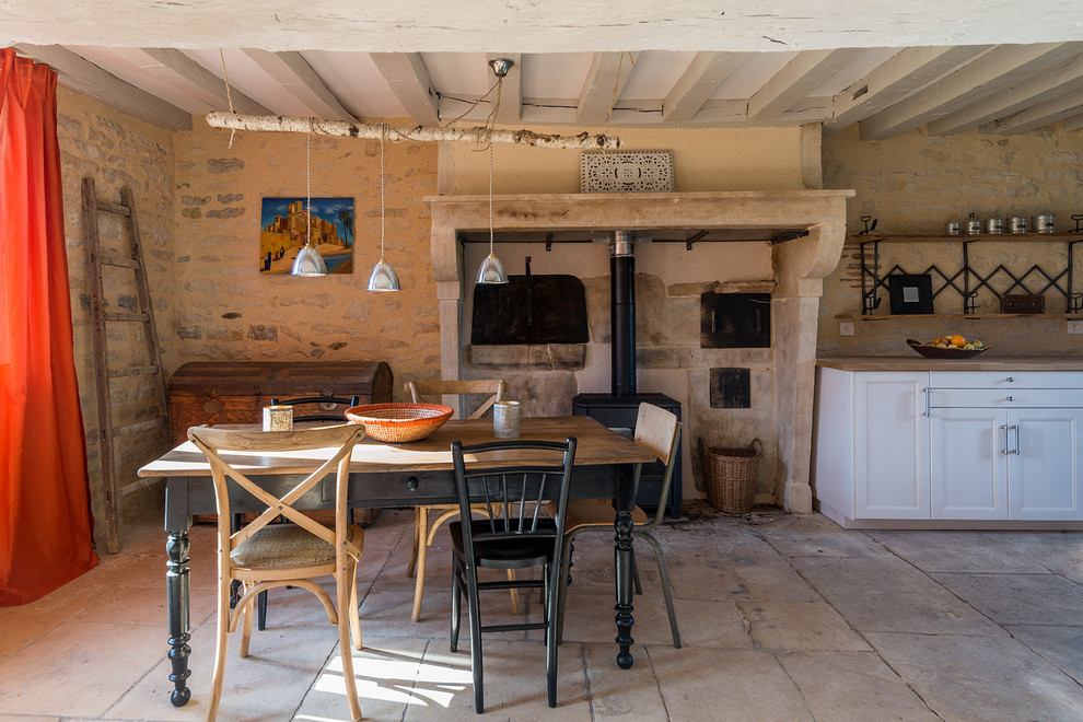 Diseño de comedor de estilo de casa de campo de tamaño medio abierto con paredes beige, estufa de leña, marco de chimenea de piedra y suelo beige