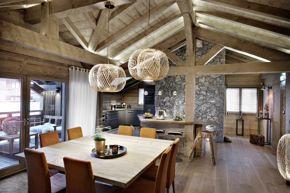 Cette image montre une grande salle à manger ouverte sur le salon chalet avec un mur gris, un sol en bois brun et aucune cheminée.