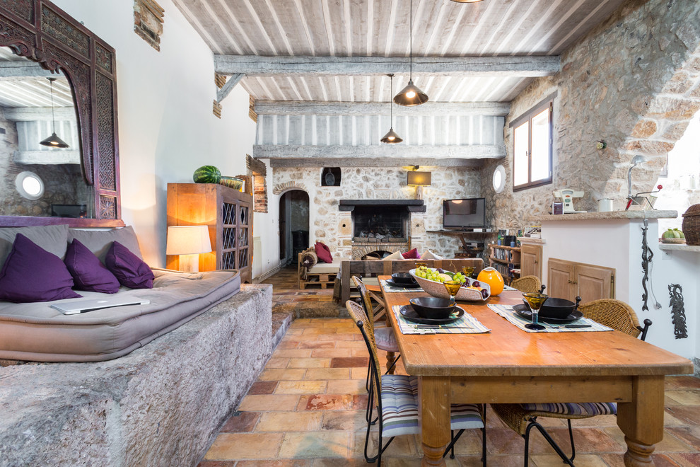 Inspiration pour une grande salle à manger ouverte sur le salon rustique avec un mur blanc, une cheminée standard, un manteau de cheminée en pierre, tomettes au sol et éclairage.