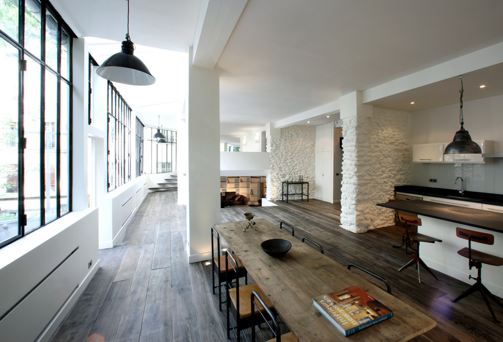 На фото: большая гостиная-столовая в стиле лофт с белыми стенами, темным паркетным полом и коричневым полом без камина