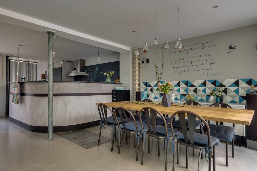 Aménagement d'une salle à manger ouverte sur la cuisine industrielle avec un mur gris, sol en béton ciré et un sol gris.