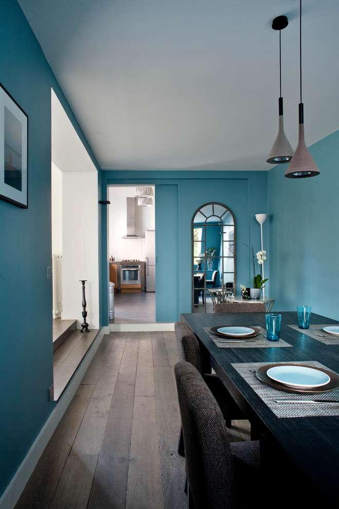 Aménagement d'une salle à manger ouverte sur le salon contemporaine avec un mur bleu, parquet foncé et un sol marron.