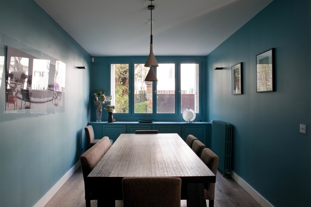 Cette image montre une salle à manger design avec parquet foncé, un sol marron et un mur bleu.