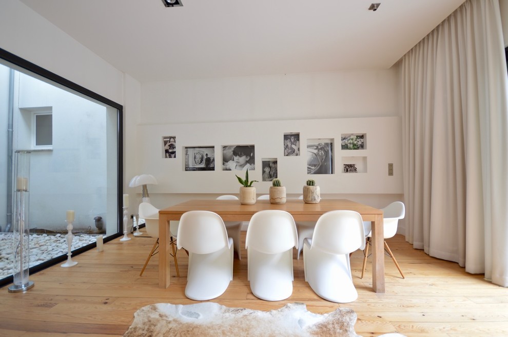 Cette image montre une salle à manger design avec un mur blanc, un sol en bois brun, un sol marron et éclairage.