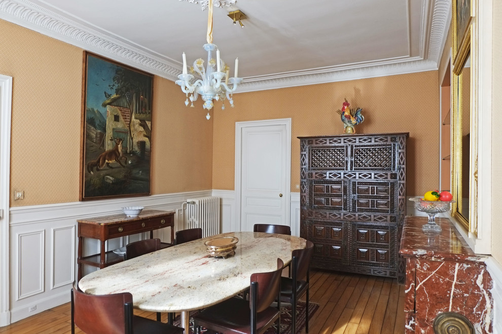 Cette image montre une salle à manger traditionnelle fermée et de taille moyenne avec un mur orange, un sol en bois brun, une cheminée standard et un manteau de cheminée en pierre.