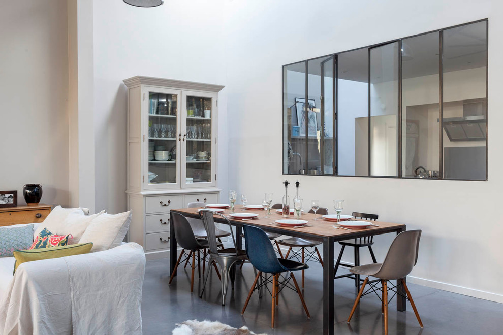 Cette image montre une grande salle à manger ouverte sur le salon urbaine avec un mur blanc, sol en béton ciré, cheminée suspendue, un manteau de cheminée en métal et un sol gris.