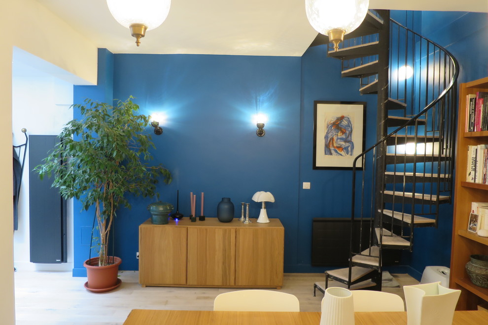 Idee per una sala da pranzo aperta verso la cucina minimal di medie dimensioni con pareti blu, parquet chiaro, camino ad angolo, cornice del camino in mattoni e pavimento beige