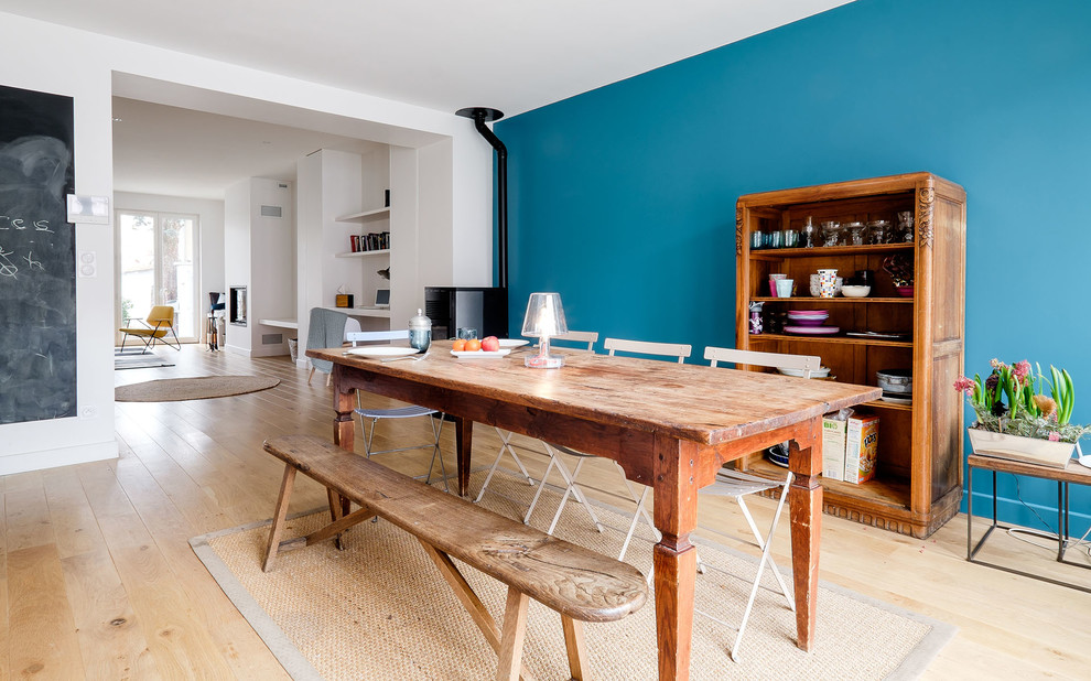 Imagen de comedor ecléctico abierto con suelo de madera clara, paredes azules y estufa de leña