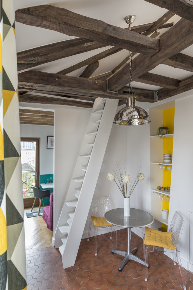 Idée de décoration pour une petite salle à manger design avec un mur jaune et tomettes au sol.