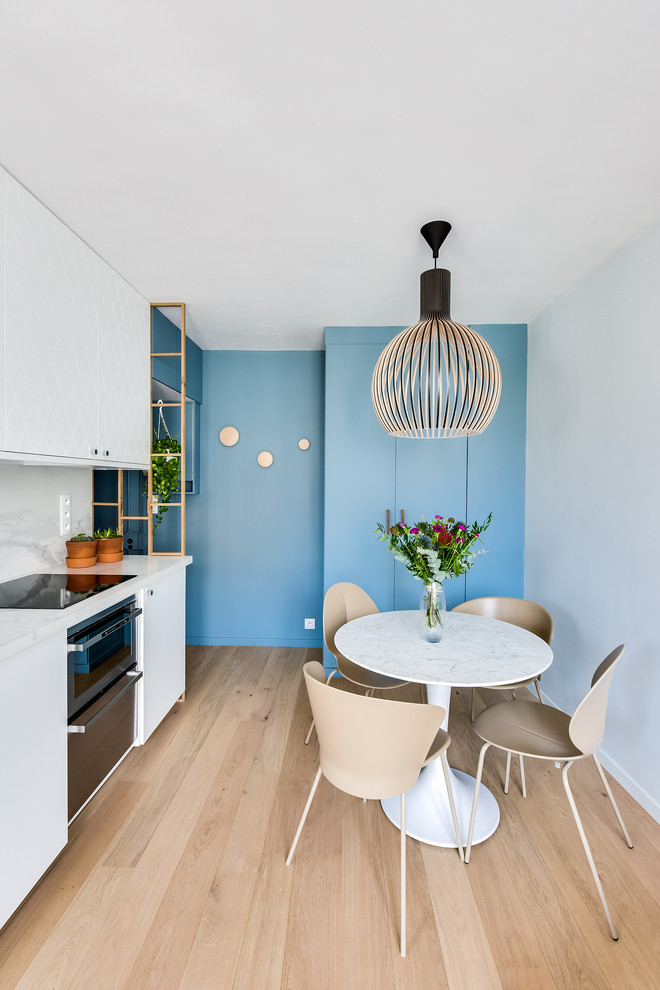 Cette photo montre une petite salle à manger ouverte sur la cuisine tendance avec un mur bleu, parquet clair et un sol beige.