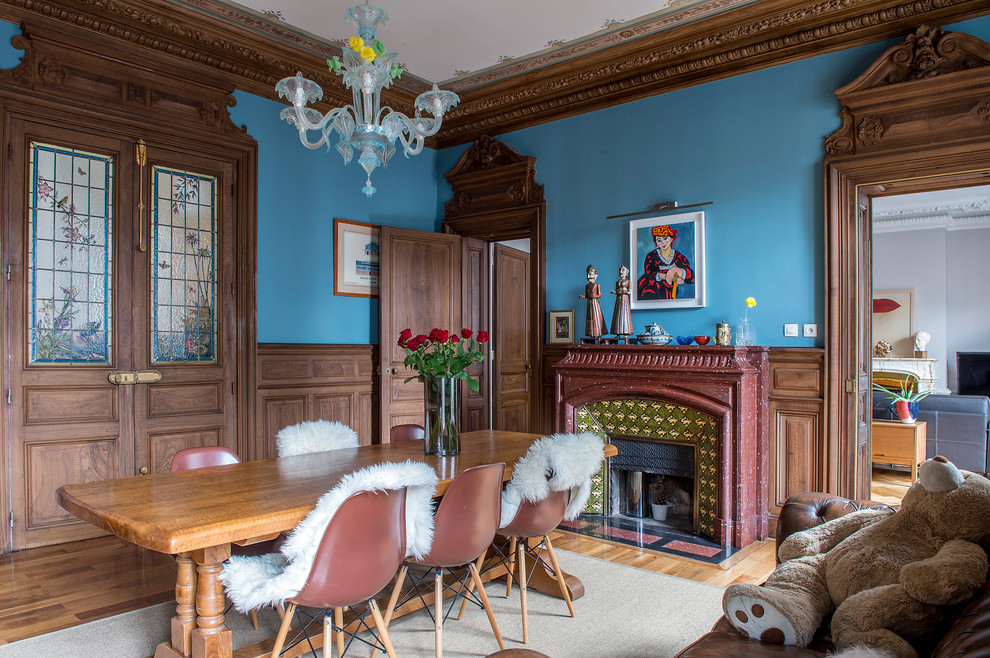 Cette image montre une salle à manger bohème fermée avec un mur bleu, parquet clair, une cheminée standard et un manteau de cheminée en carrelage.