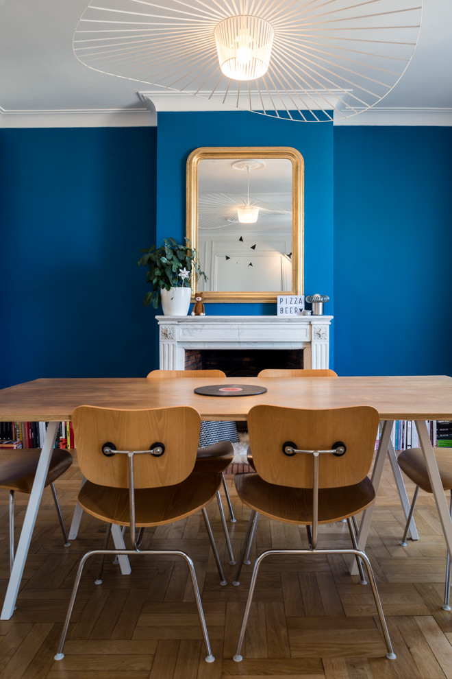 Inspiration pour une grande salle à manger ouverte sur le salon design avec un sol en bois brun, une cheminée standard, un manteau de cheminée en pierre, un mur bleu et un sol marron.