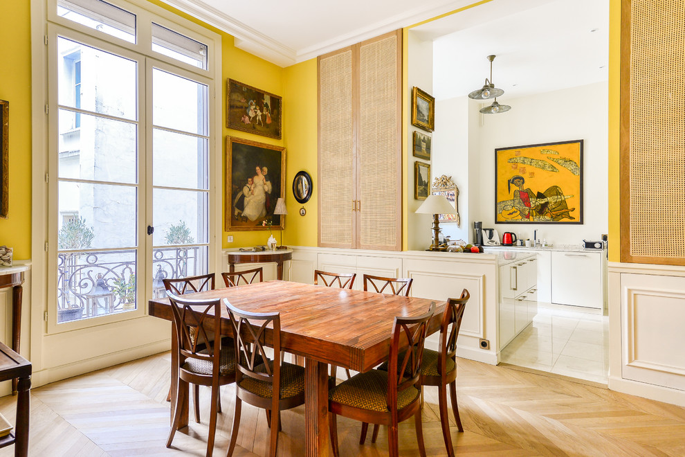 Aménagement d'une salle à manger ouverte sur le salon classique avec un mur jaune, parquet clair, un sol marron et éclairage.