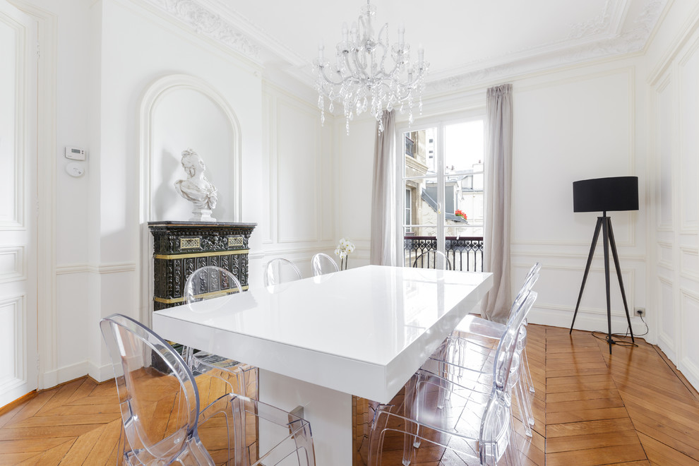 This is an example of a large bohemian enclosed dining room in Paris with white walls, medium hardwood flooring, a standard fireplace and feature lighting.