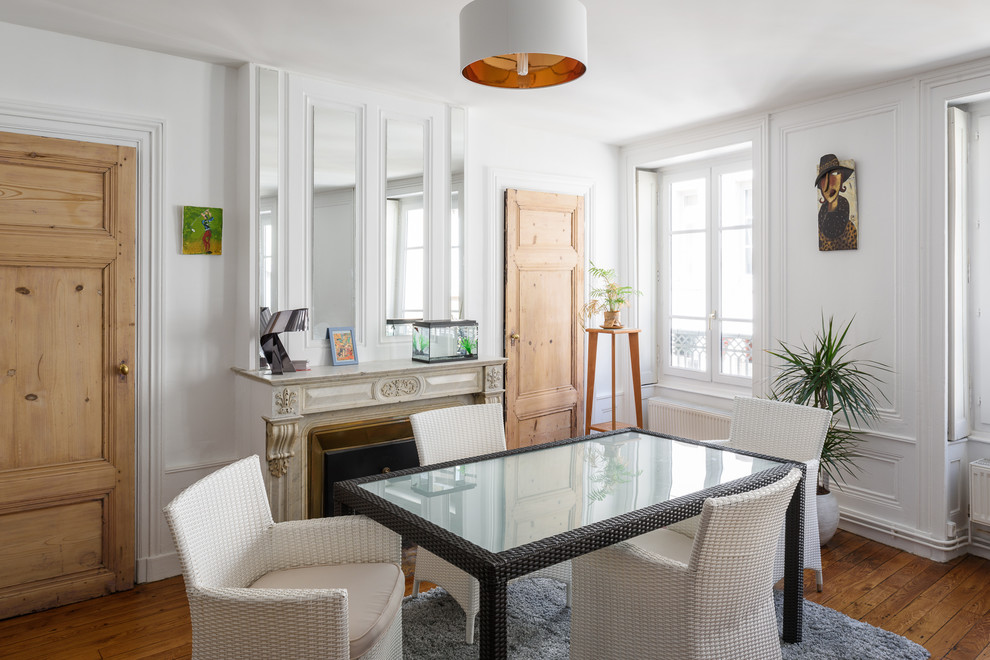 Idées déco pour une salle à manger contemporaine fermée avec un mur blanc, un sol en bois brun et une cheminée standard.