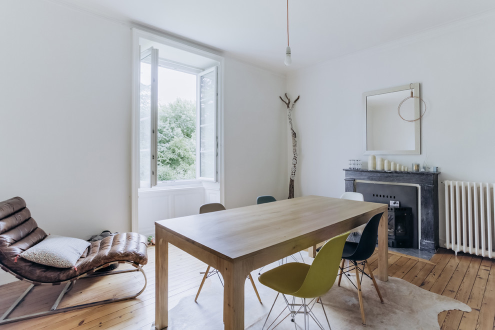 Photo of a scandinavian enclosed dining room in Nantes with white walls, light hardwood flooring, a standard fireplace and a wooden fireplace surround.