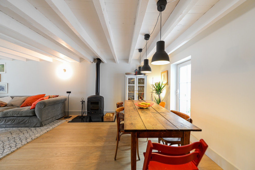 Cette photo montre une salle à manger ouverte sur le salon tendance de taille moyenne avec parquet clair, un poêle à bois, un sol beige et un mur blanc.