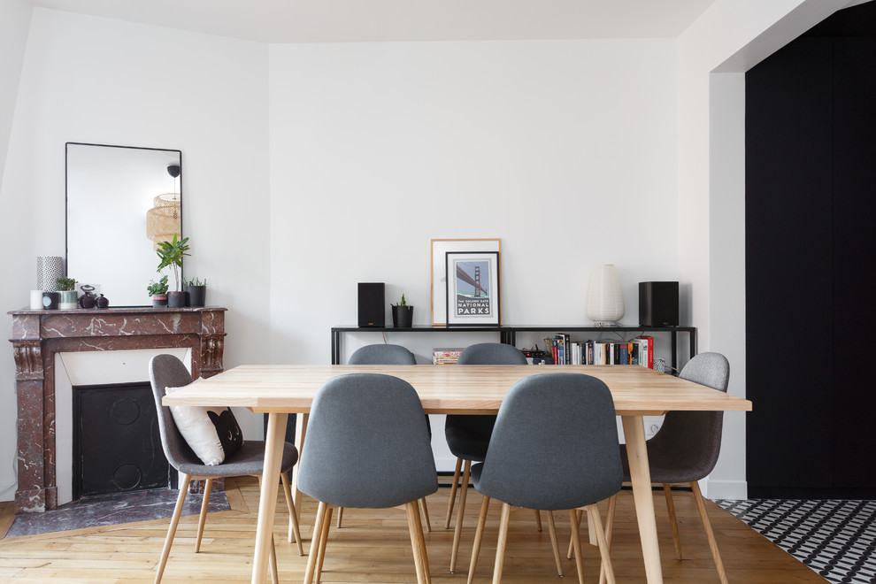 Réalisation d'une salle à manger ouverte sur le salon design de taille moyenne avec un mur blanc, un sol en bois brun, une cheminée standard, un sol marron et un manteau de cheminée en pierre.