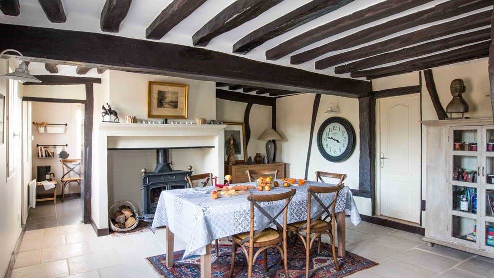 Exemple d'une salle à manger nature fermée et de taille moyenne avec un mur beige, tomettes au sol, un poêle à bois, un manteau de cheminée en brique et un sol beige.