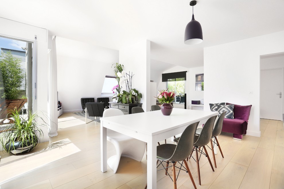 This is an example of a medium sized contemporary dining room in Paris with white walls, light hardwood flooring and no fireplace.
