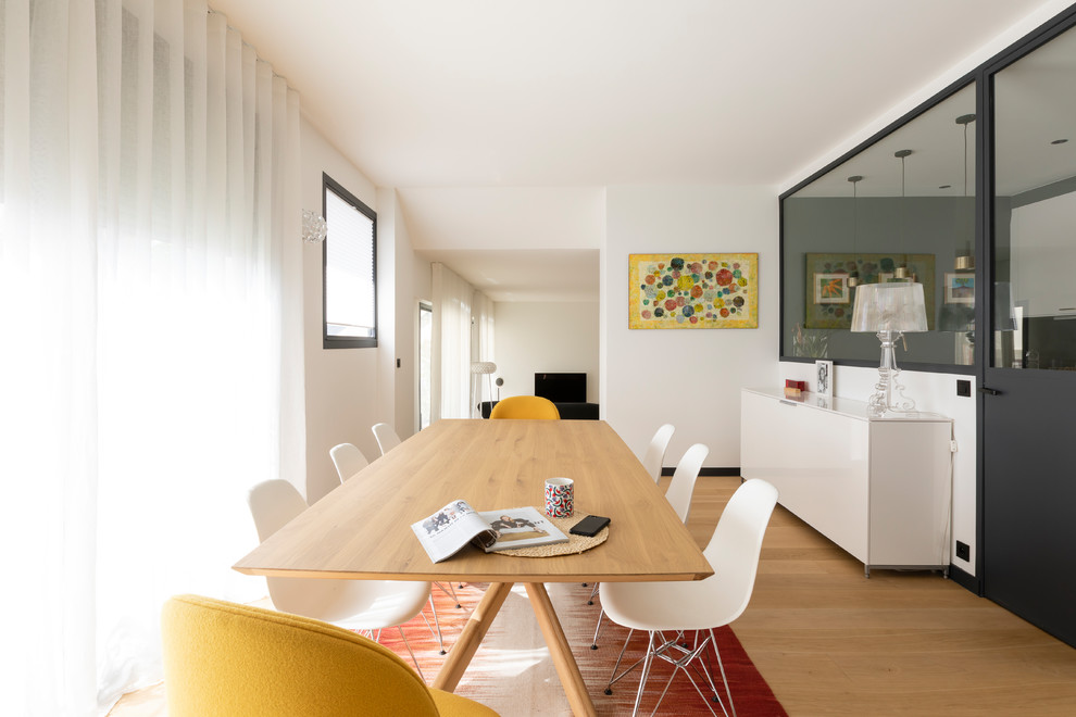 This is an example of a medium sized contemporary open plan dining room in Paris with white walls, light hardwood flooring, a standard fireplace and feature lighting.