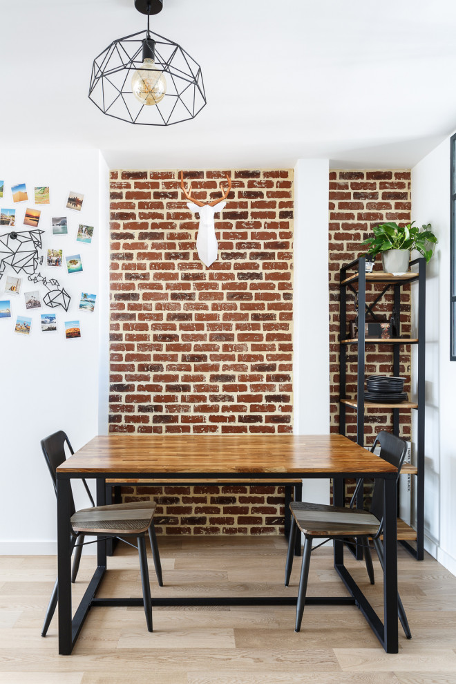 This is an example of a small urban open plan dining room in Paris with white walls, light hardwood flooring, no fireplace, beige floors and brick walls.