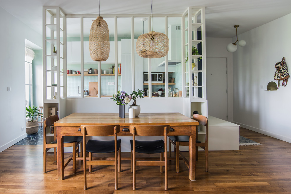Cette photo montre une salle à manger ouverte sur la cuisine tendance de taille moyenne avec un mur blanc, un sol en bois brun et un sol marron.