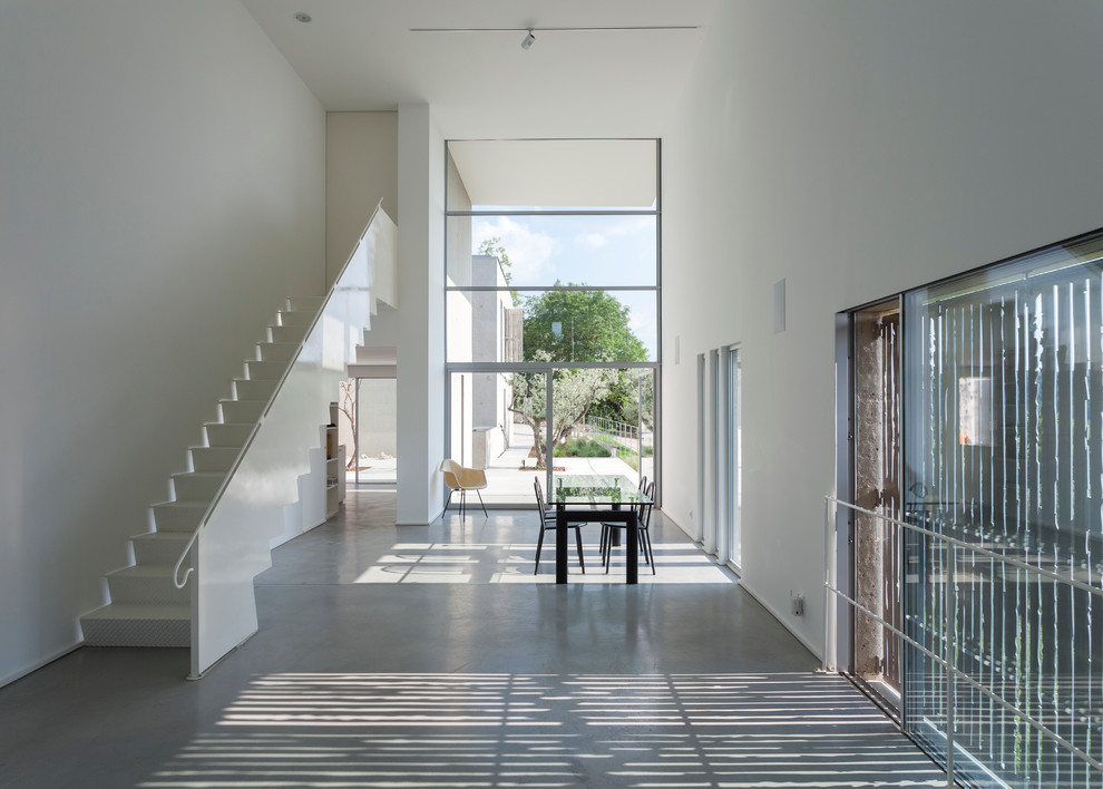 Esempio di un'ampia sala da pranzo aperta verso il soggiorno minimal con pareti bianche, pavimento in cemento e nessun camino