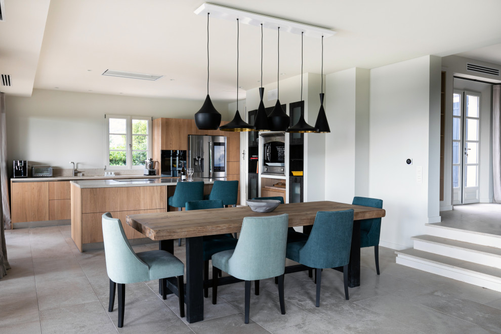 Cette photo montre une grande salle à manger ouverte sur la cuisine tendance avec un mur blanc et un sol gris.