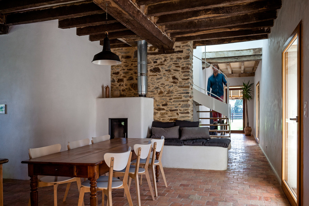 Cette photo montre une salle à manger nature de taille moyenne avec un mur blanc, tomettes au sol et un poêle à bois.