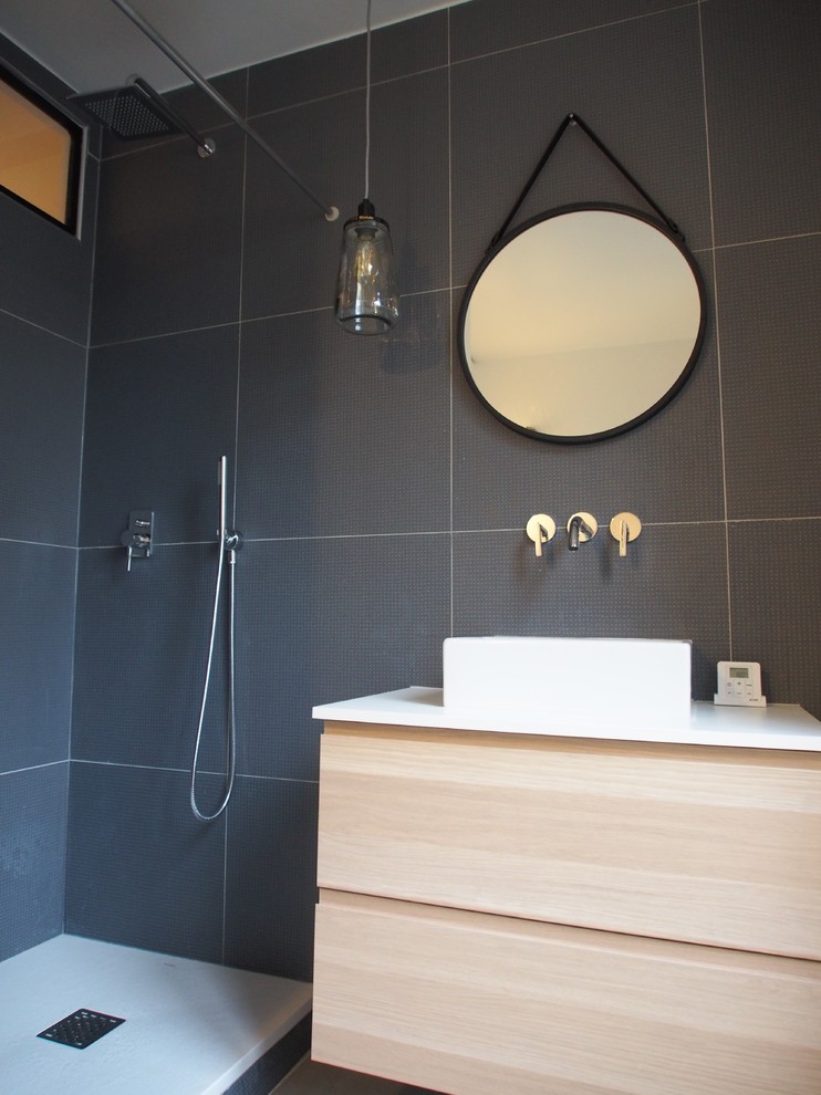 Foto på ett mellanstort funkis en-suite badrum, med skåp i ljust trä, en kantlös dusch, en vägghängd toalettstol, blå kakel, keramikplattor, vita väggar, klinkergolv i keramik, ett fristående handfat och laminatbänkskiva