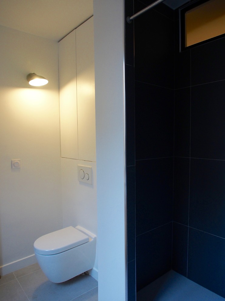 This is an example of a medium sized contemporary ensuite bathroom in Paris with light wood cabinets, a built-in shower, a wall mounted toilet, blue tiles, ceramic tiles, white walls, ceramic flooring, a vessel sink and laminate worktops.