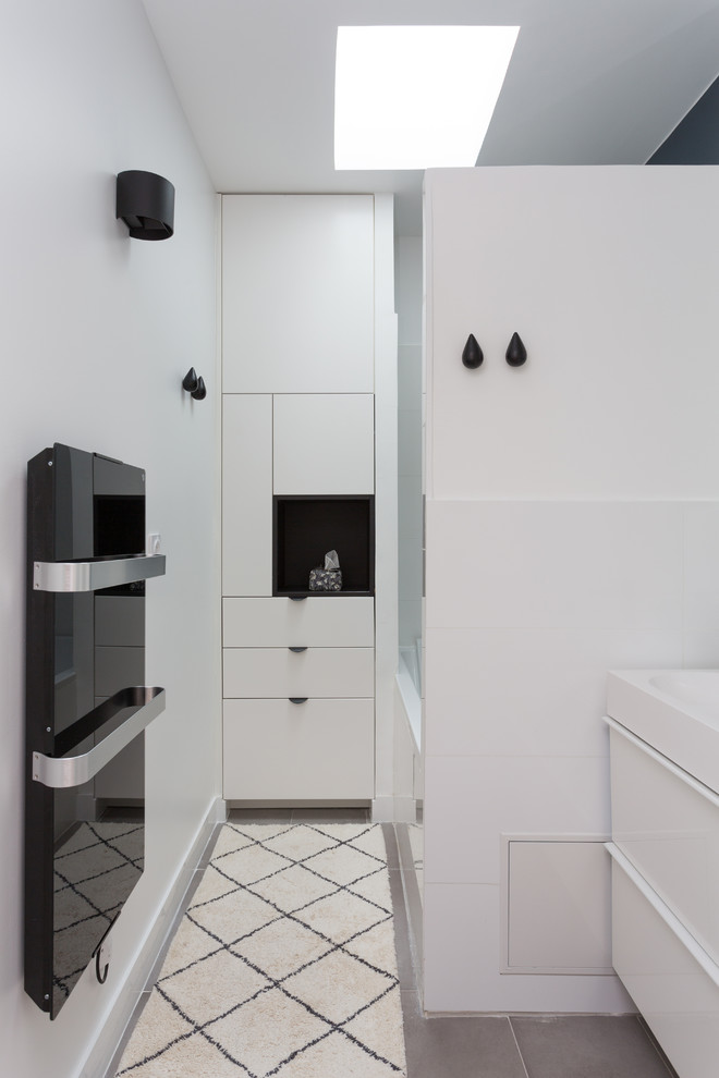 Inspiration for a medium sized classic ensuite bathroom in Paris with white walls, flat-panel cabinets, white cabinets, an alcove bath, a shower/bath combination, a two-piece toilet, white tiles, porcelain tiles, ceramic flooring, a trough sink, solid surface worktops, grey floors, an open shower and white worktops.