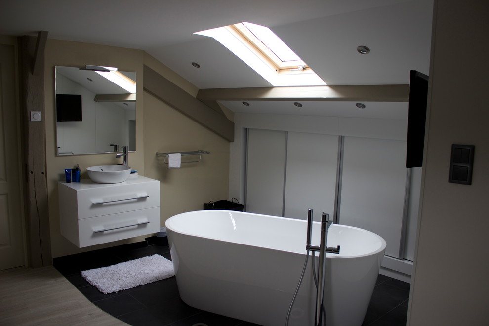 Cette photo montre une grande salle de bain éclectique avec une baignoire indépendante, un carrelage gris, un mur beige, un plan vasque et un sol gris.