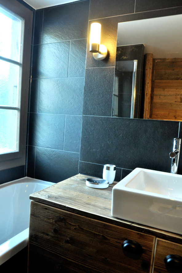 Réalisation d'une salle de bain chalet en bois vieilli avec une vasque, un placard à porte plane, un plan de toilette en bois, une baignoire encastrée, un carrelage noir, des dalles de pierre, un mur noir et un sol en ardoise.