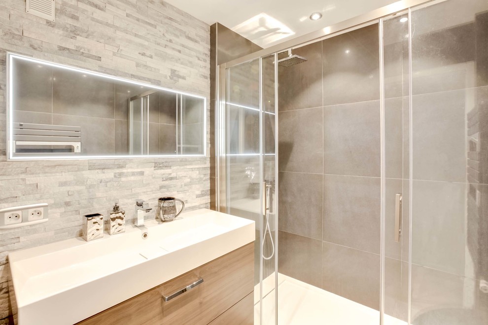 Idéer för ett litet modernt badrum med dusch, med skåp i ljust trä, en kantlös dusch, grå kakel, stenhäll, grå väggar, klinkergolv i keramik, bänkskiva i akrylsten, grått golv och dusch med skjutdörr