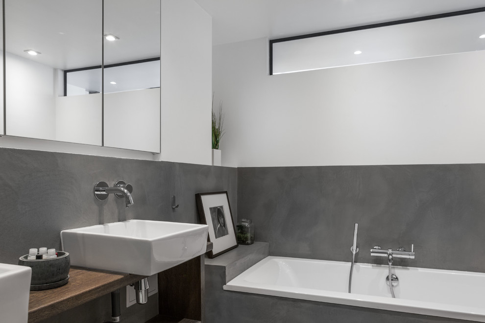 Cette image montre une salle de bain principale design de taille moyenne avec une baignoire posée, un mur gris, une vasque et un plan de toilette en bois.