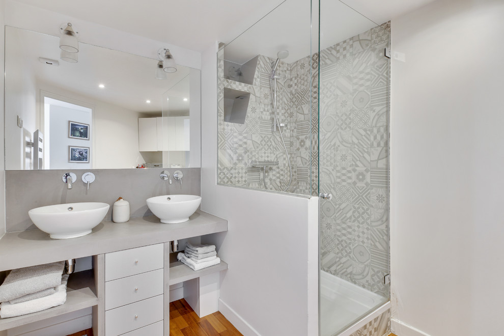 Foto på ett funkis grå badrum, med släta luckor, vita skåp, en hörndusch, grå kakel, grå väggar, mellanmörkt trägolv, ett fristående handfat, brunt golv och dusch med gångjärnsdörr