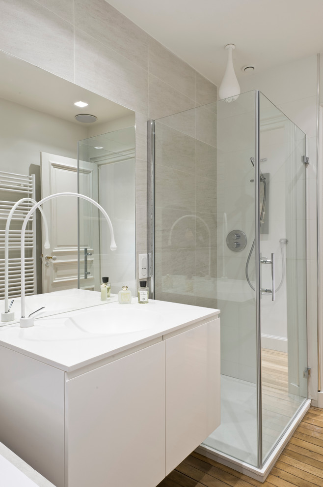 Aménagement d'une salle de bain principale contemporaine de taille moyenne avec un lavabo intégré, un placard à porte plane, des portes de placard blanches, une douche d'angle, un sol en bois brun et un mur gris.