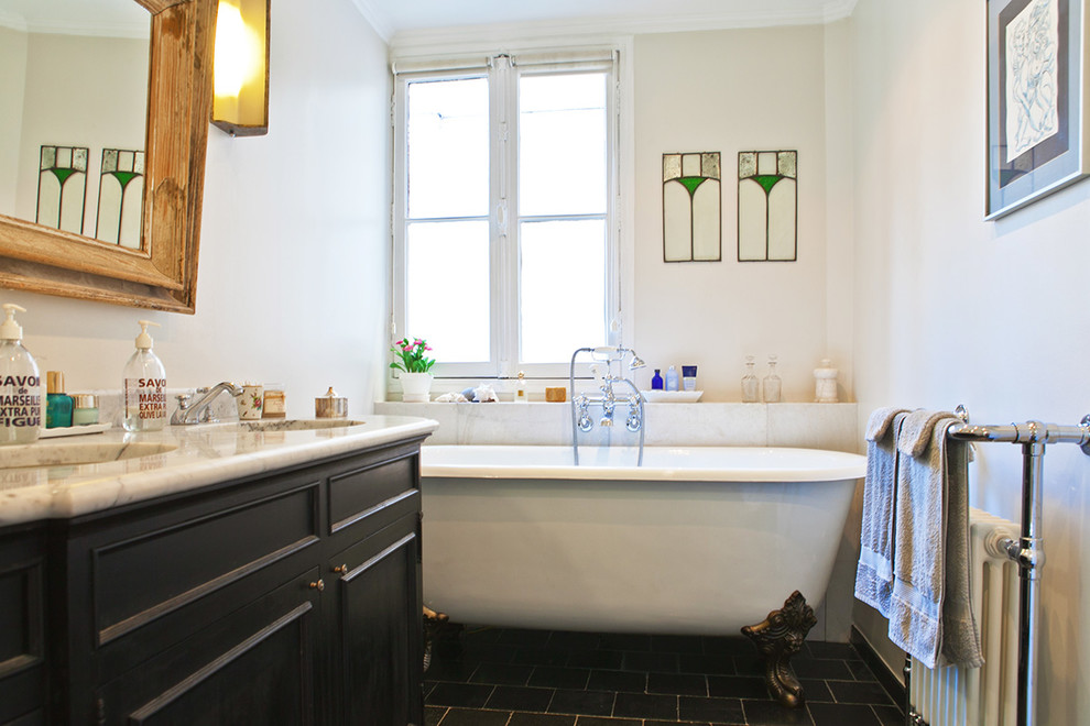 Foto på ett mellanstort vintage vit en-suite badrum, med luckor med profilerade fronter, svarta skåp, ett badkar med tassar, en dusch/badkar-kombination, en toalettstol med separat cisternkåpa, vit kakel, marmorkakel, grå väggar, ett fristående handfat, marmorbänkskiva, grått golv och med dusch som är öppen