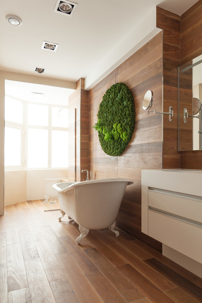 Cette photo montre une salle de bain principale tendance de taille moyenne avec des portes de placard blanches, une baignoire sur pieds et un sol en bois brun.