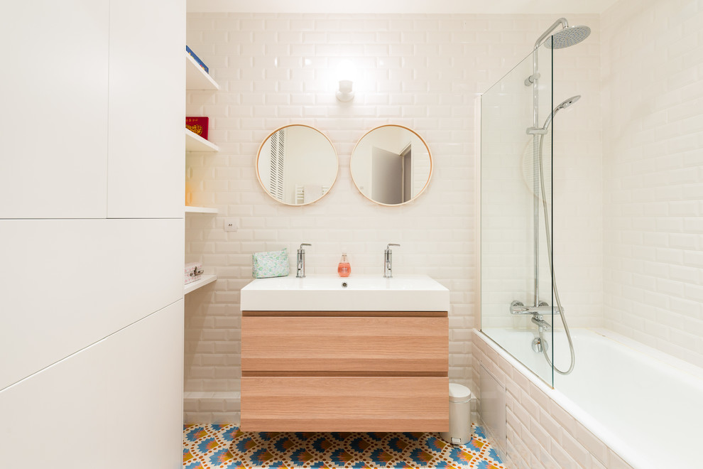 На фото: ванная комната среднего размера в скандинавском стиле с керамической плиткой, белыми стенами, полом из цементной плитки, консольной раковиной, плоскими фасадами, светлыми деревянными фасадами, душем над ванной, белой плиткой, разноцветным полом, открытым душем, ванной в нише и душевой кабиной с