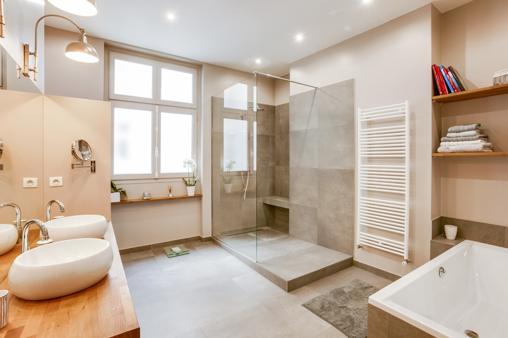 Cette image montre une grande salle de bain principale minimaliste avec une baignoire en alcôve, une douche à l'italienne, WC suspendus, un carrelage gris, des carreaux de porcelaine, un mur gris, carreaux de ciment au sol, un lavabo posé, un plan de toilette en bois et un sol gris.