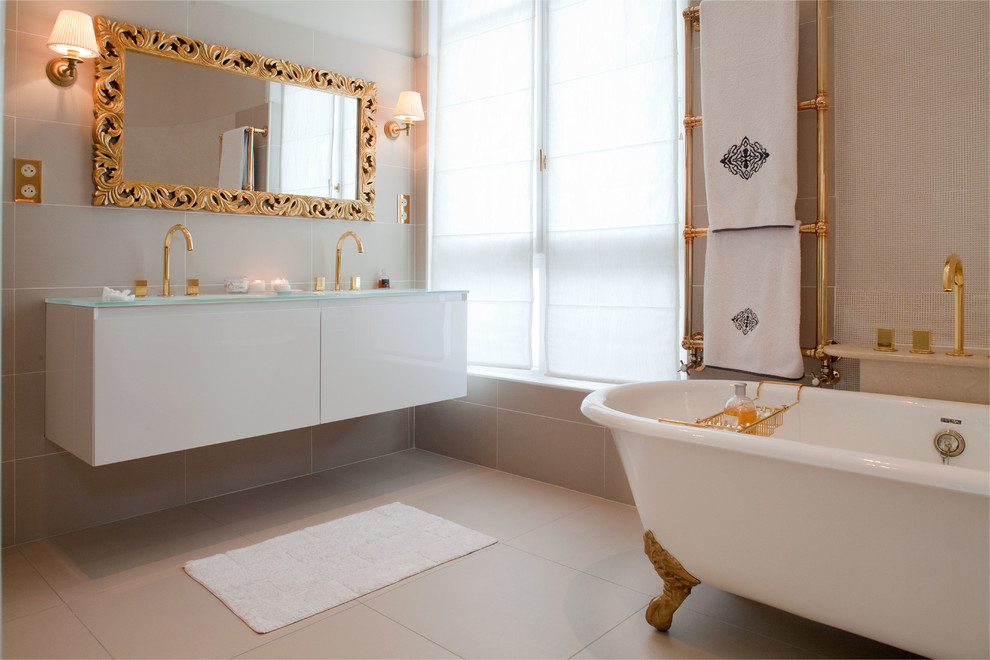 На фото: главная ванная комната среднего размера в современном стиле с белыми фасадами, ванной на ножках, бежевыми стенами, стеклянной столешницей, бежевой плиткой, керамической плиткой, полом из керамической плитки, подвесной раковиной и бежевым полом