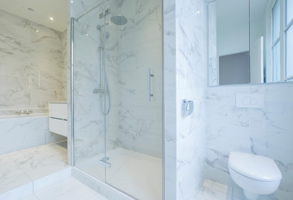 Imagen de cuarto de baño principal actual de tamaño medio con puertas de armario blancas, bañera encastrada, ducha empotrada, sanitario de pared, baldosas y/o azulejos azules, baldosas y/o azulejos grises y suelo de mármol